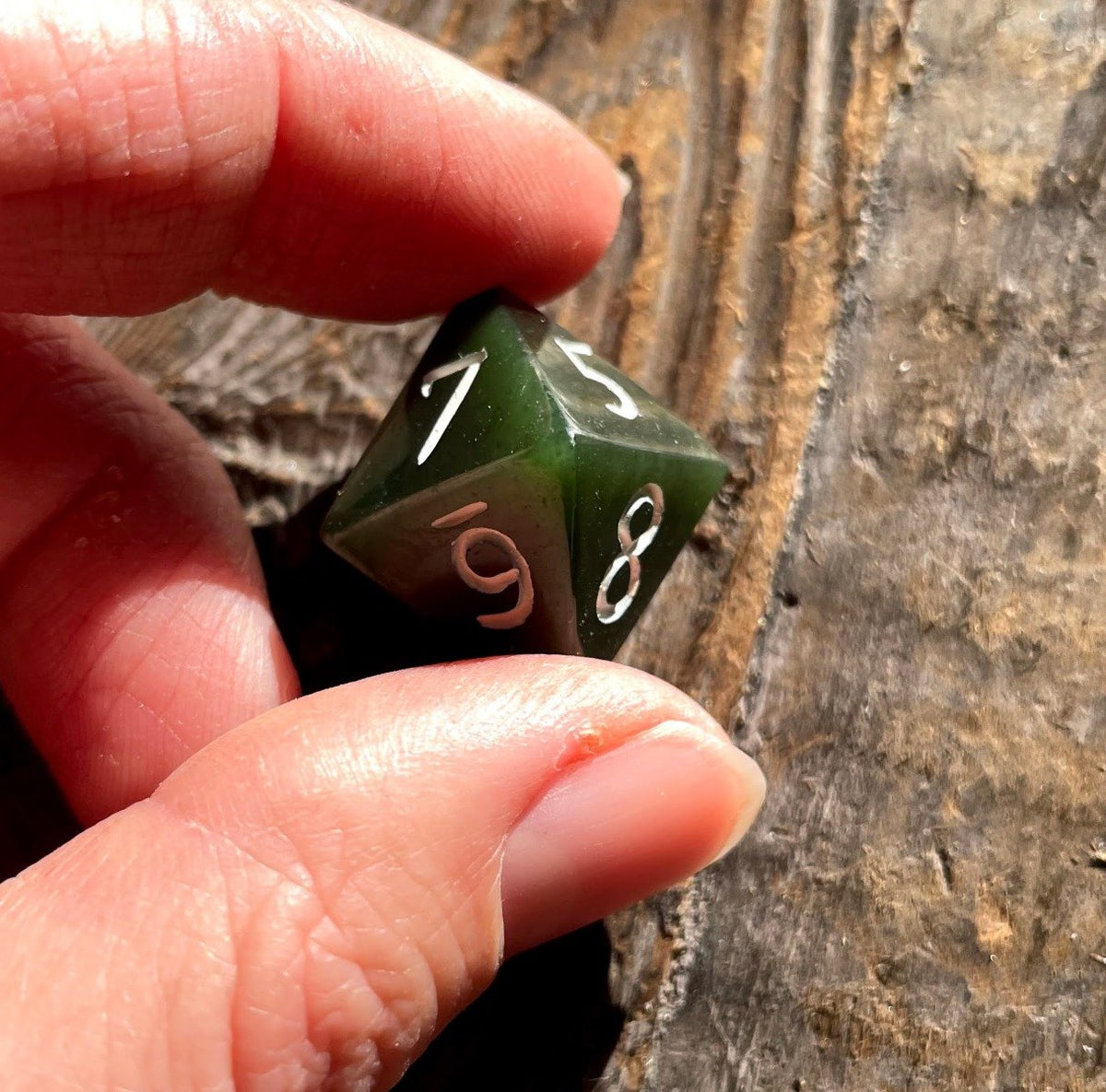 Hand holds green jade D8 die with white numerals on a rustic wooden background