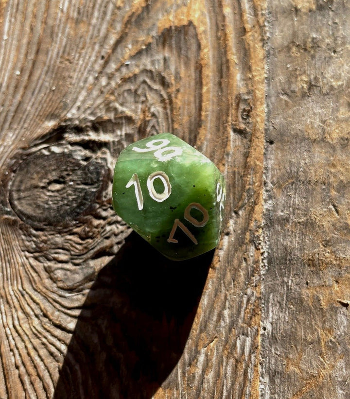 Green jade D10 percentile die on a weathered wooden surface showing 00 and 10 faces.