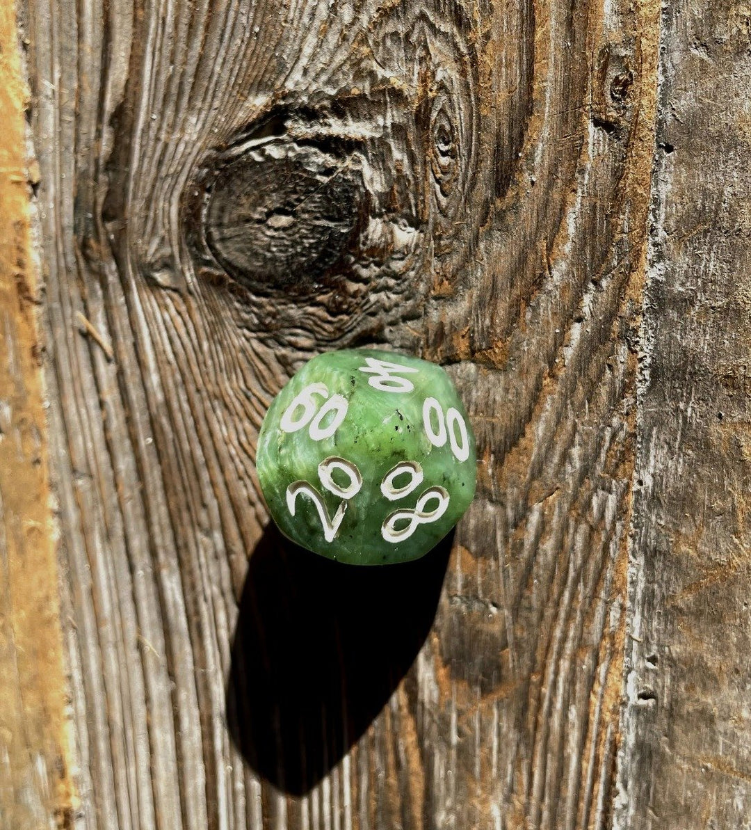 Green jade die resting on a textured weathered wooden surface.