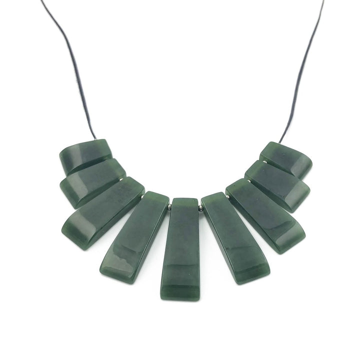 Close up of jade necklace showing large green rectangular beads arranged in a curved collar on a black cord.