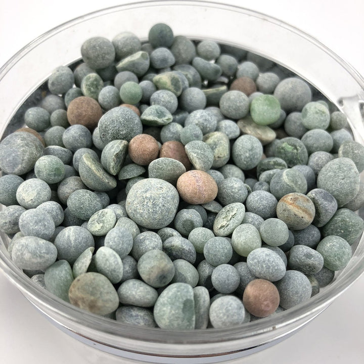 Close-up of assorted green gray rounded aquarium beads in a glass container.