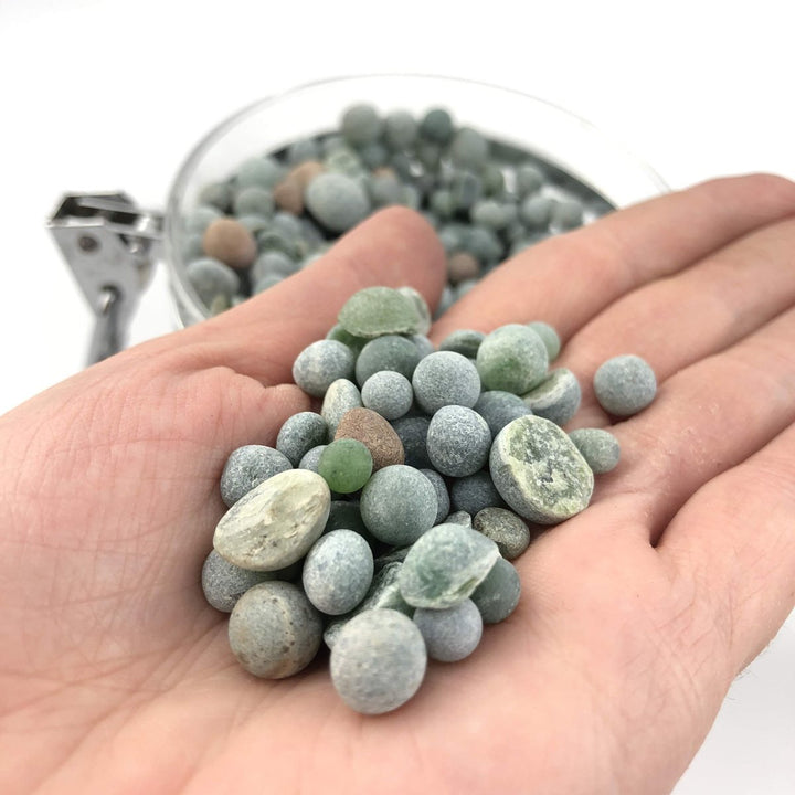 Small green and gray aquarium beads held in an open hand with a bead filled bowl in the background