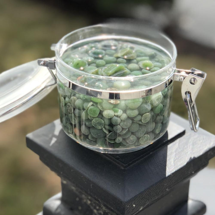 Green aquarium beads in a glass jar perched on a black pedestal outdoors