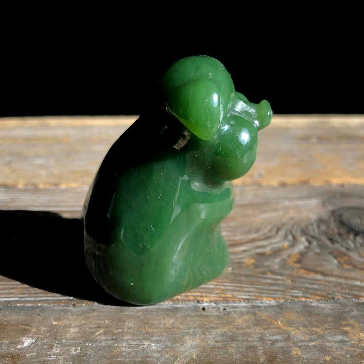 Side view of a jade green pig figurine on a weathered wooden surface with a dark backdrop