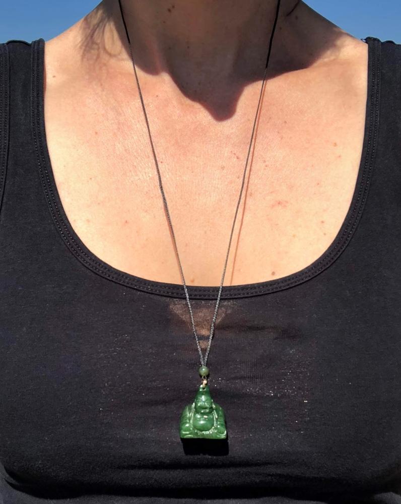 Green jade Happy Buddha pendant worn on a black cord necklace by a person