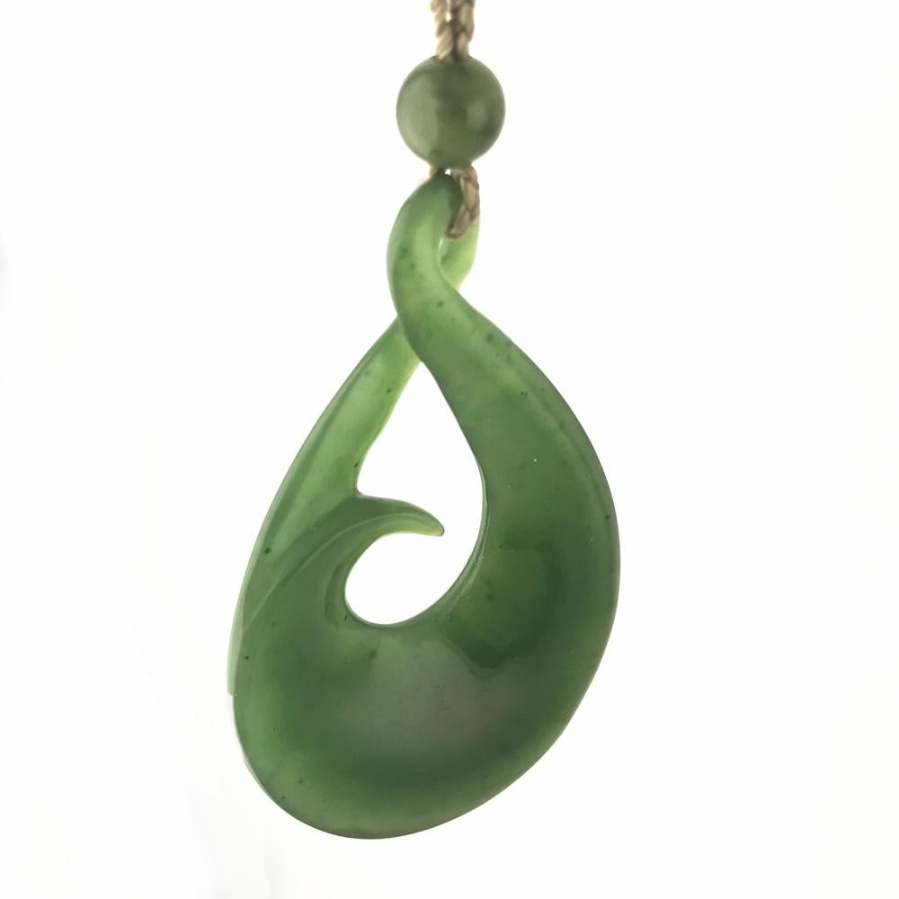 Green jade pendant with a looping teardrop shape and a small bead above, suspended from a cord.