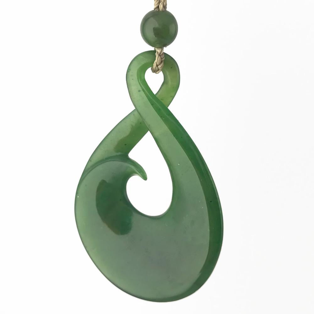 Green jade pendant with looping design and central opening, hung on a braided cord.