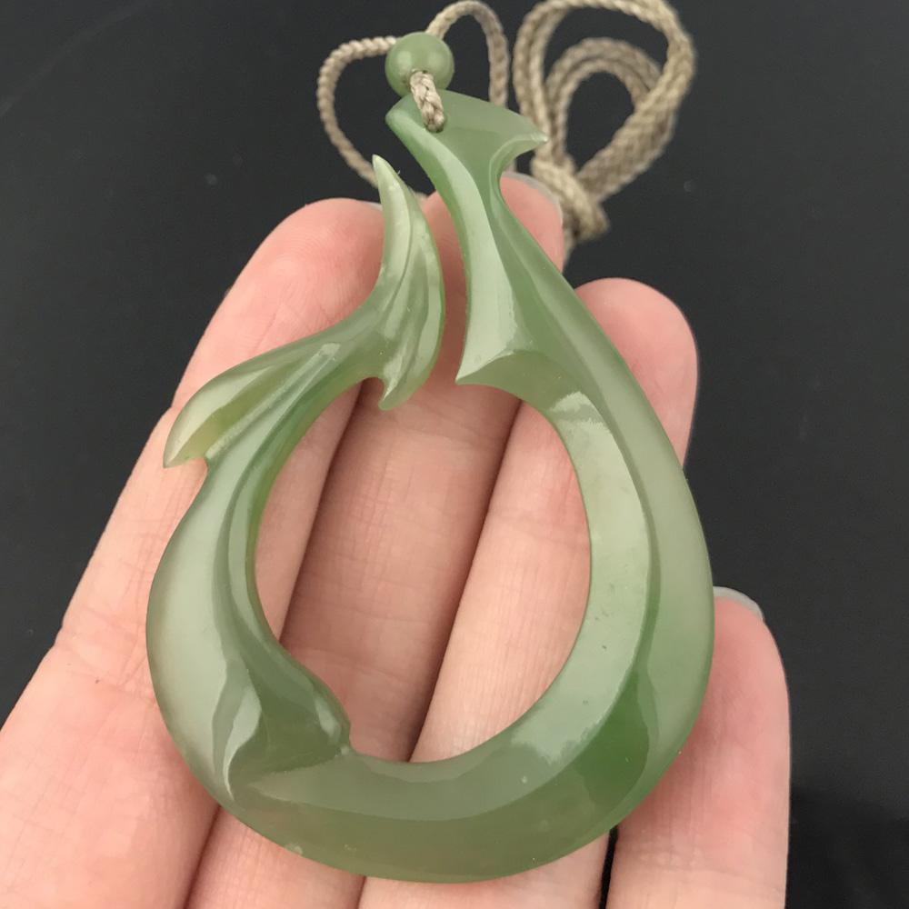 Close up of pale green jade teardrop pendant held between fingers against a dark background