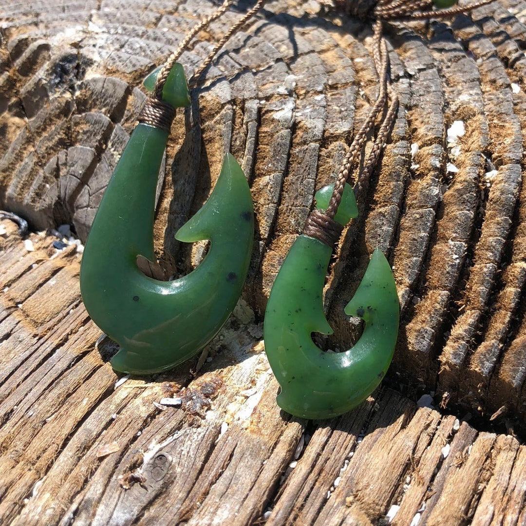 Two green jade fish hook pendants with braided cords resting on weathered wood