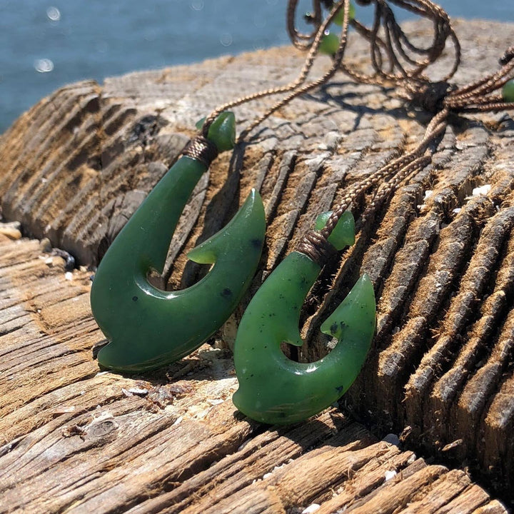 Close up of two green jade fish hook pendants with braided cords on weathered wood surface
