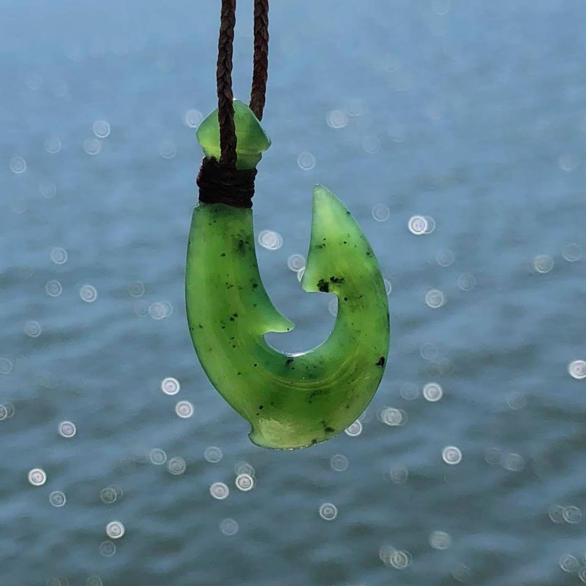 Green fish hook pendant on brown braided cord with a blue ocean background