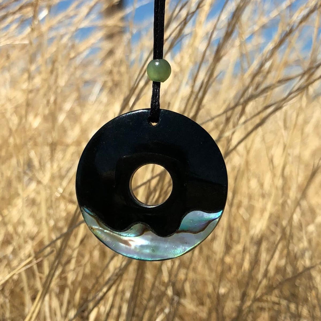 Black jade and abalone round pendant with a hole in the center, brown grass in the background