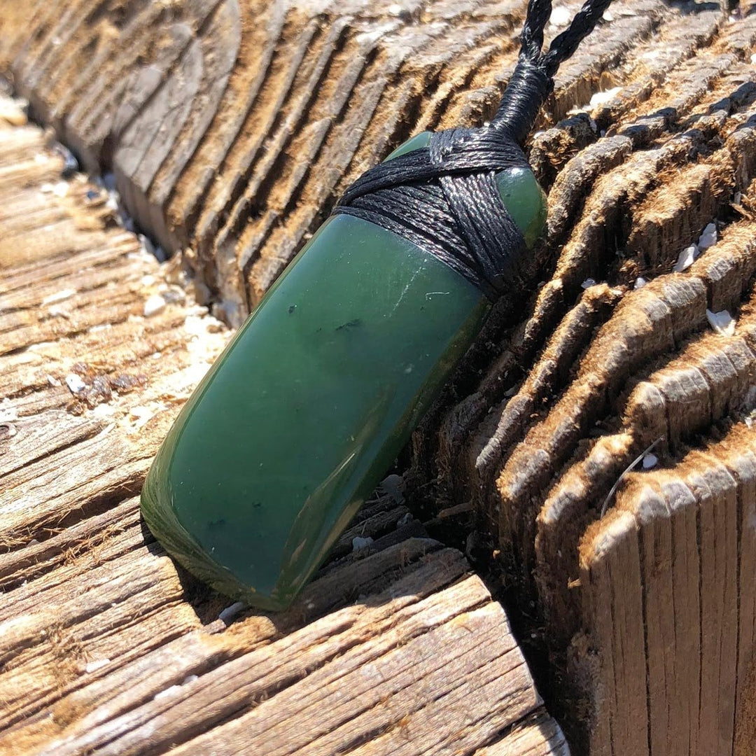 Green jade pendant wrapped in black cord resting on weathered wood.