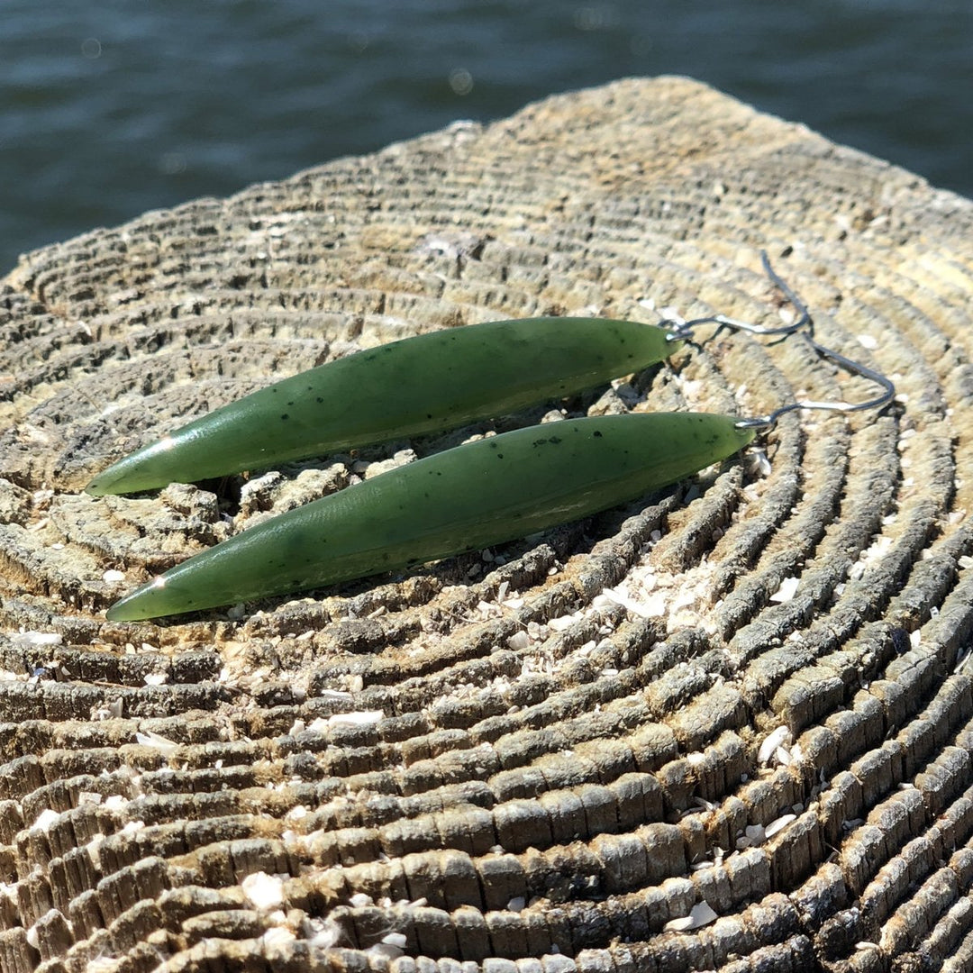 Long green jade drop earrings with silver hooks laid on a textured tree stump
