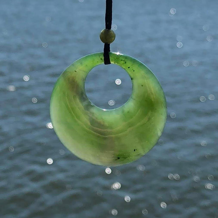 Green jade circle pendant with a central hole hanging on a black cord