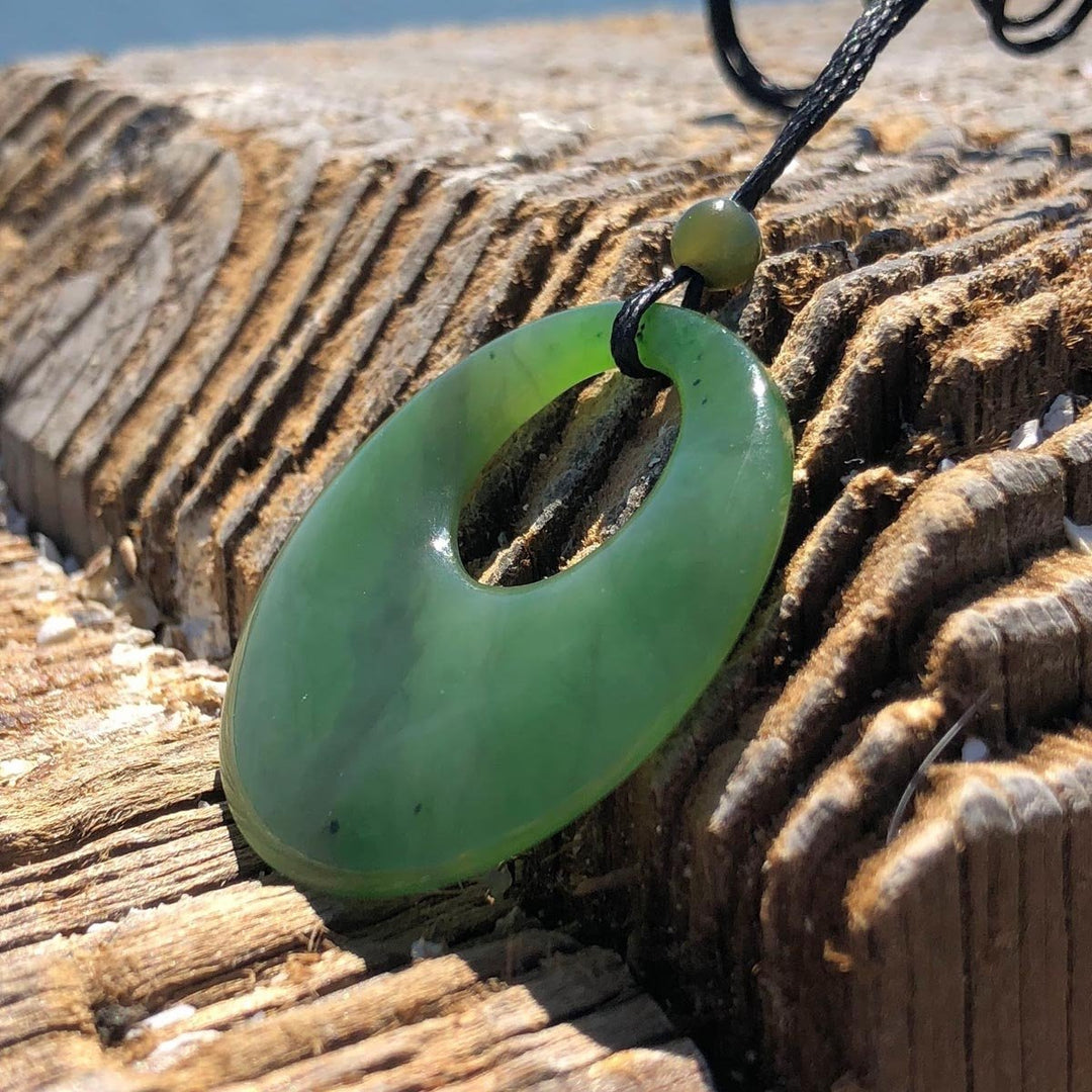 Close up of green jade circle pendant on a black cord with bead against weathered wood