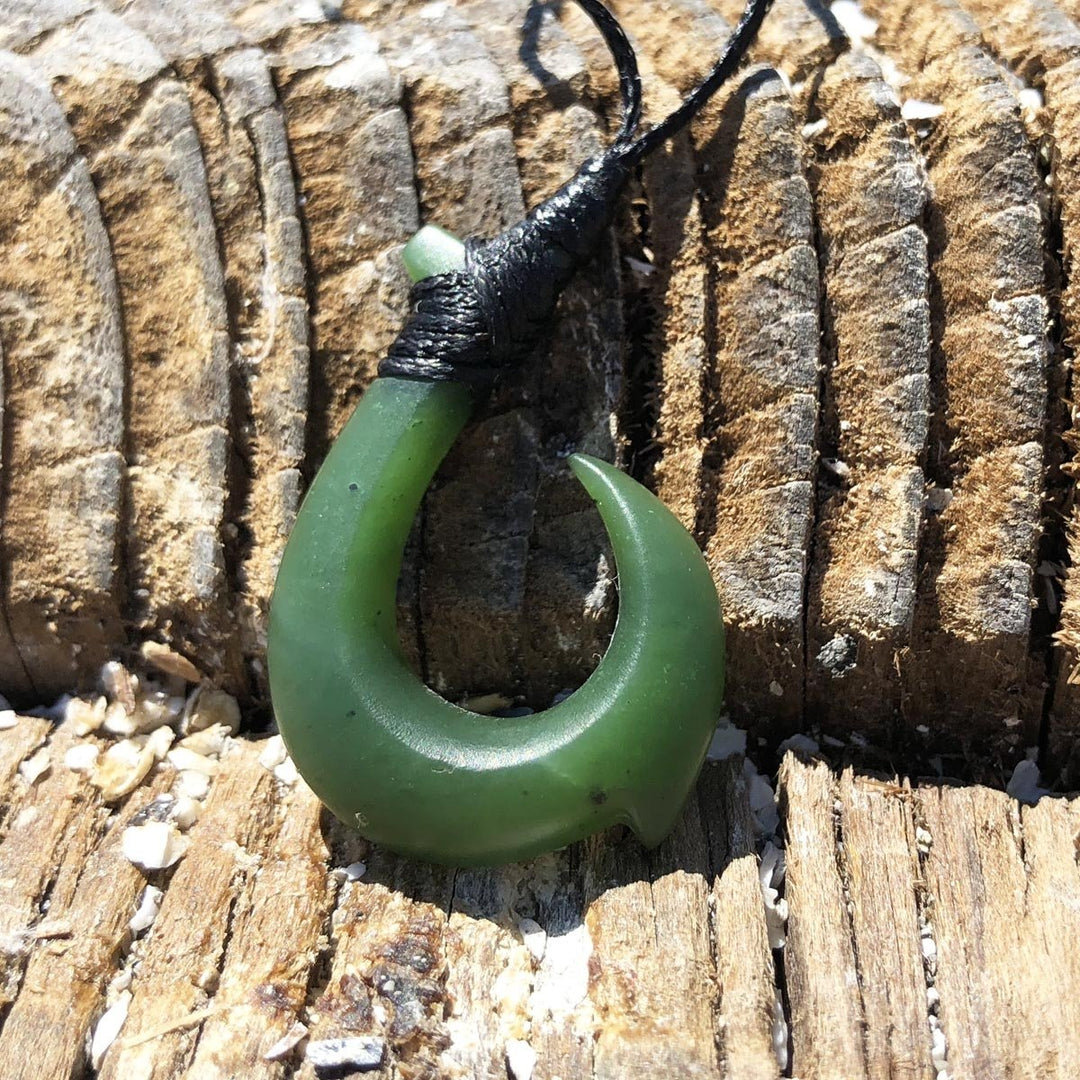 Green jade hook pendant with a curved crescent shape hanging from a black cord