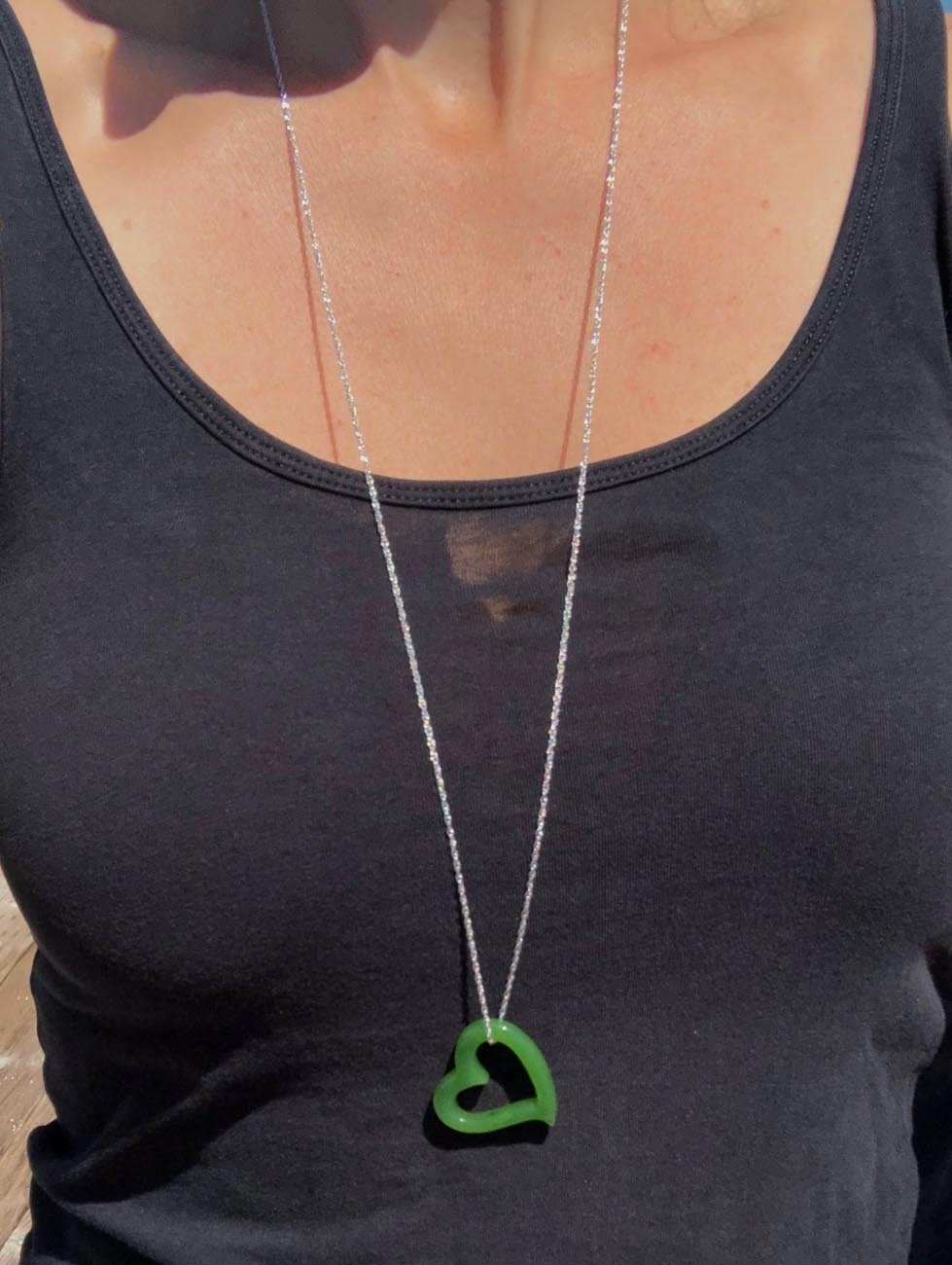 Green heart shaped pendant on a silver chain worn over a black tank top.