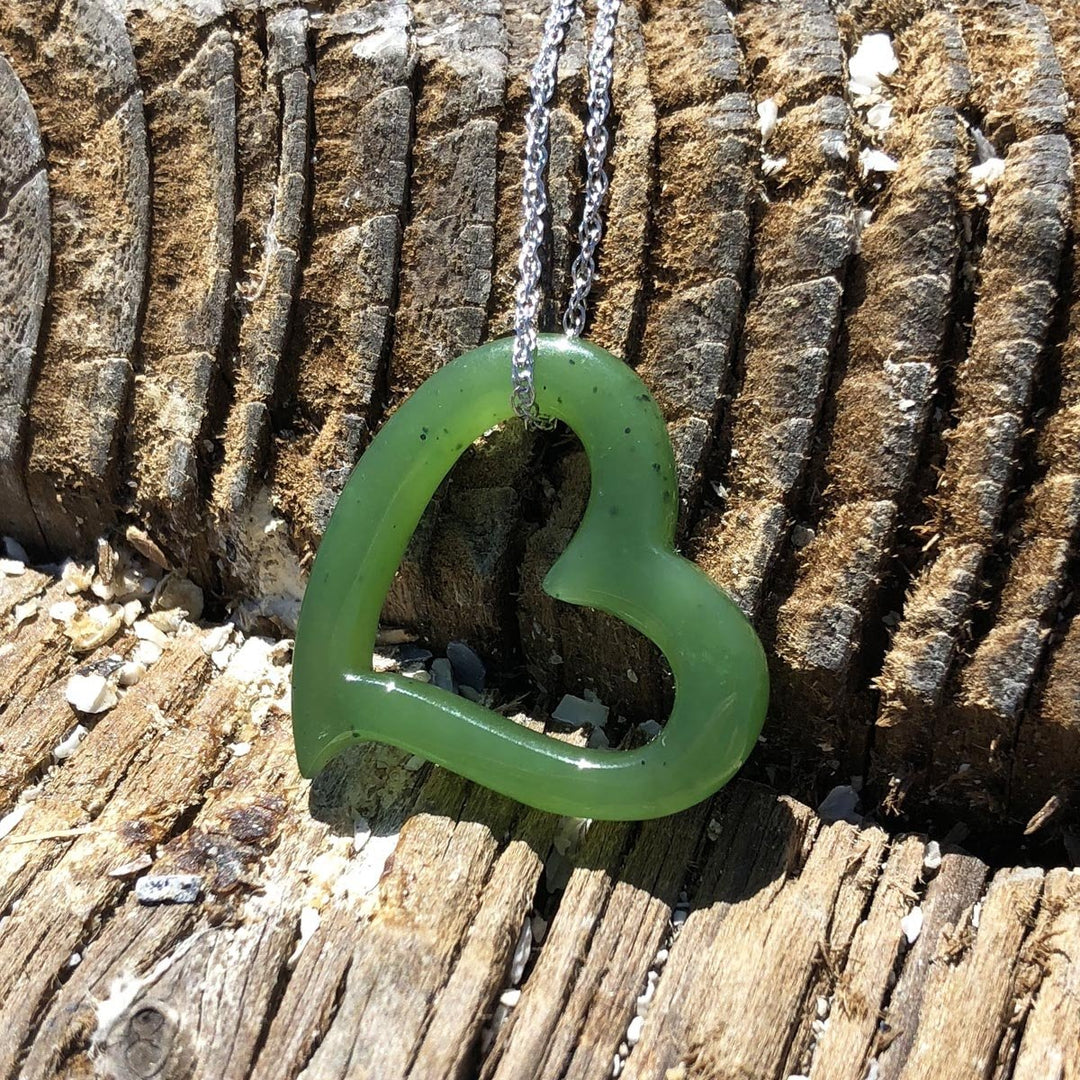 Green heart shaped pendant on a silver chain laid against weathered wood background.