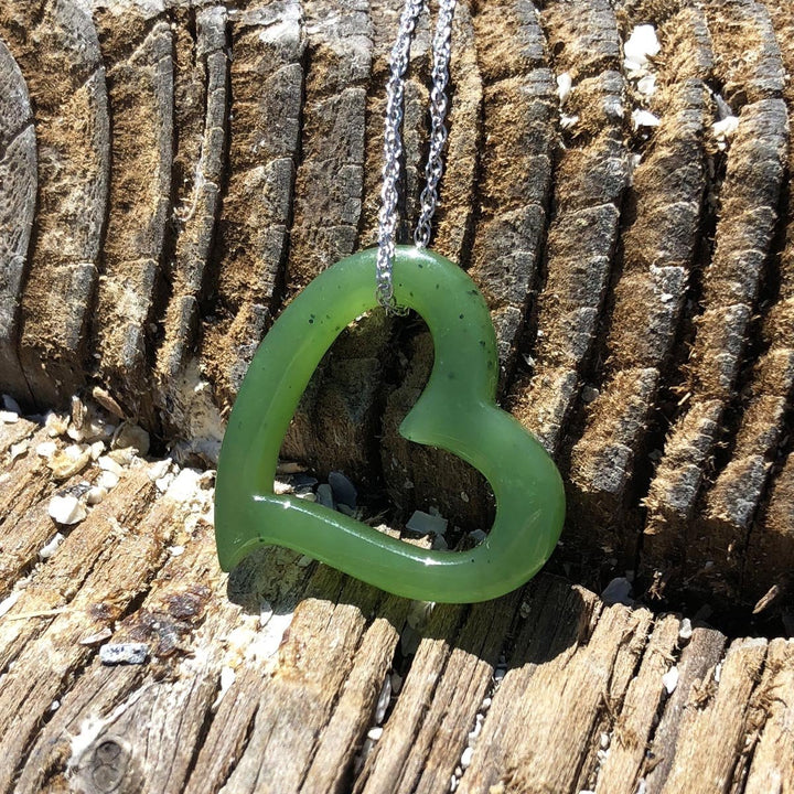 Green heart shaped pendant on a silver chain laid against weathered wood background.