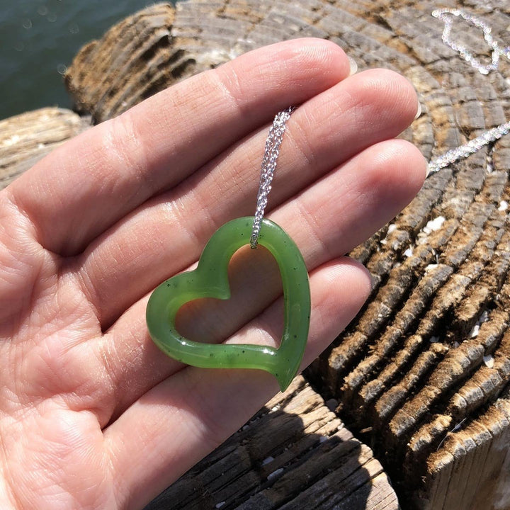 Hand holding a green heart shaped pendant on a silver chain over a weathered wooden surface.