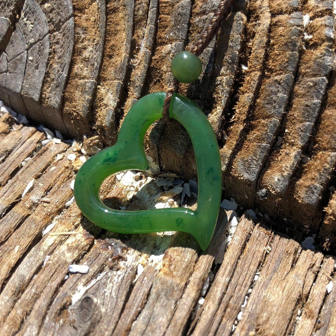 Green jade heart pendant on braided cord against weathered wood