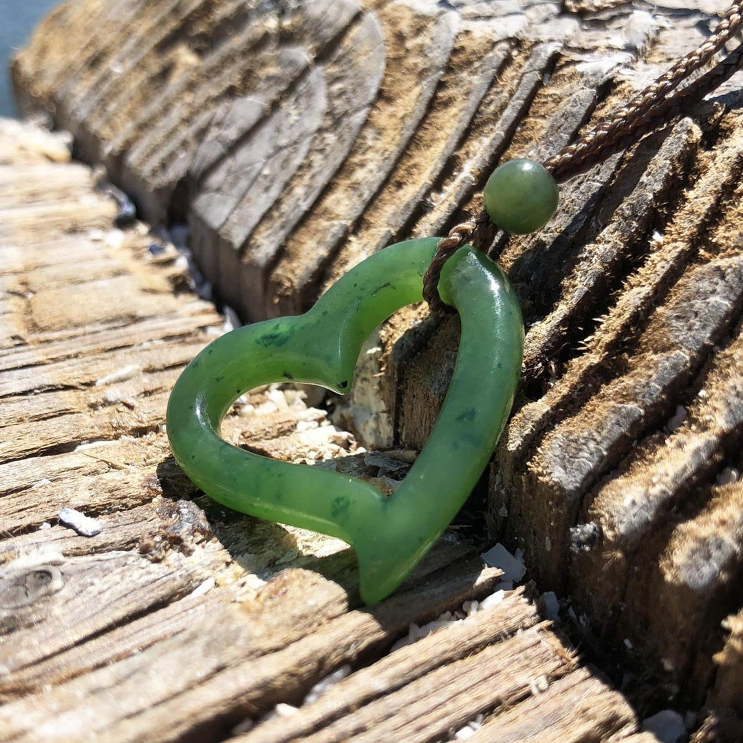 Green hollow heart pendant on a braided brown cord with bead resting on weathered driftwood