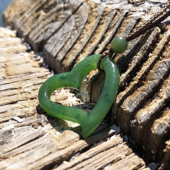 Green hollow heart pendant on a braided brown cord with bead resting on weathered driftwood