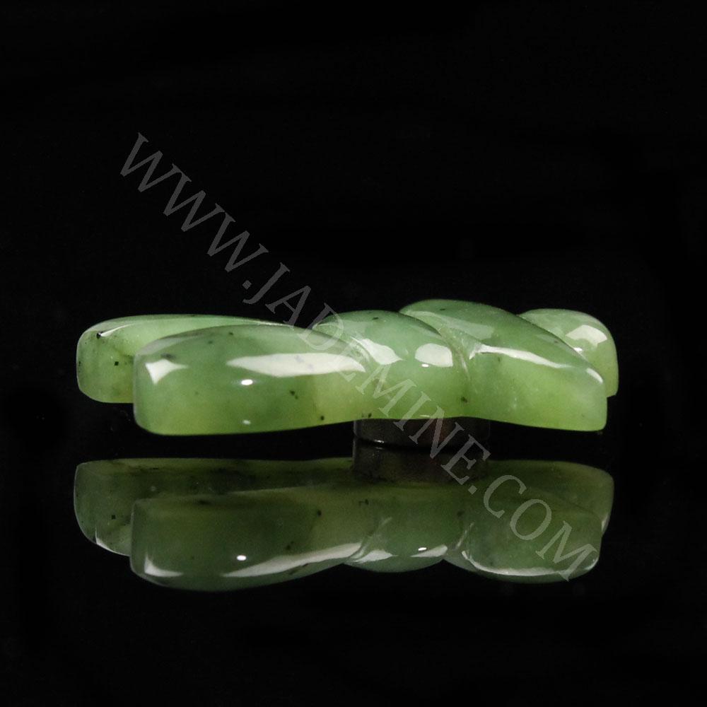 Side view of the green jade Inukshuk magnet laid flat on a black surface