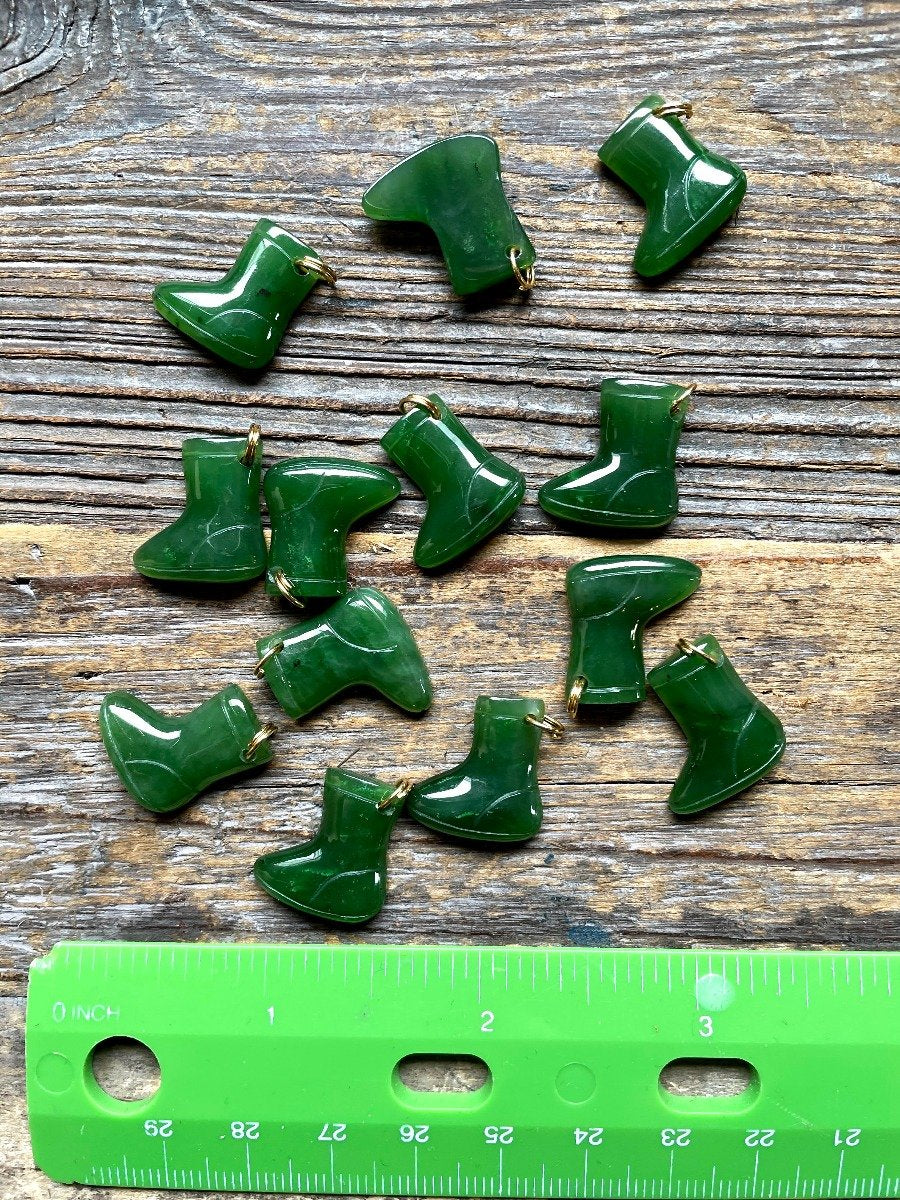 Set of green glossy snow boot charms scattered on a rustic wooden surface with a ruler for scale