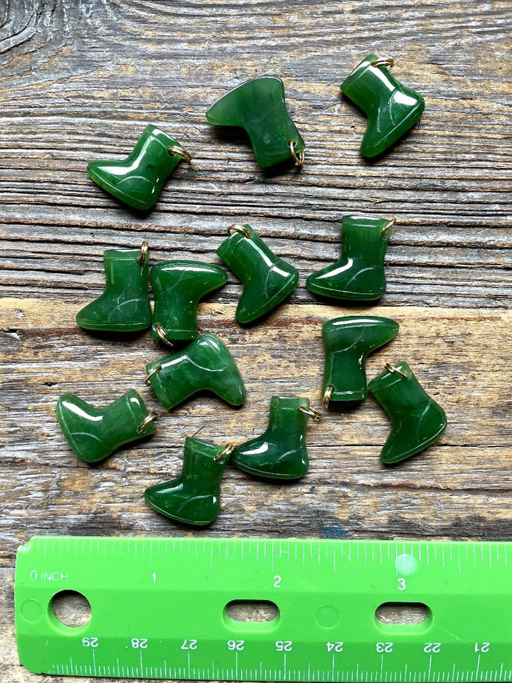 Set of green glossy snow boot charms scattered on a rustic wooden surface with a ruler for scale