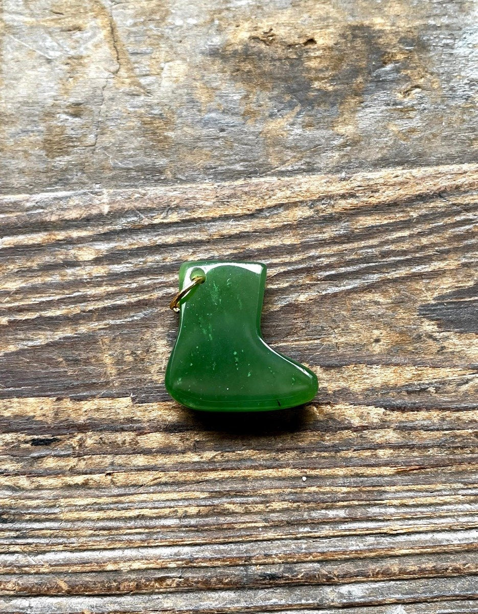Green glossy snow boot charm with a small gold loop on a weathered wooden surface