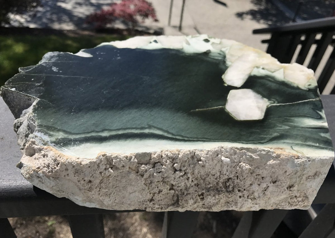 Olive Wyoming with Quartz Crystal Inclusions rock slab showing dark olive green interior and rough beige exterior.
