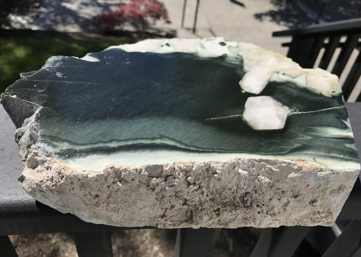 Olive Wyoming with Quartz Crystal Inclusions rock slab showing dark olive green interior and rough beige exterior.