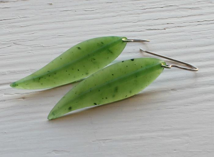 Two green leaf shaped earrings with silver hooks on a white surface