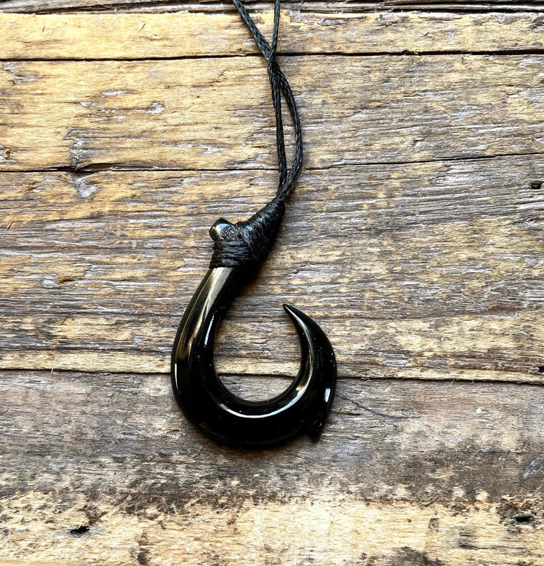 Black jade fish hook pendant displayed on rustic wooden surface with a knotted black cord above