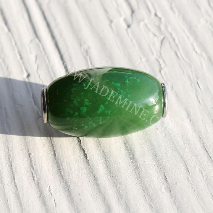 Oval green jade bead with a polished surface and silver end caps on a light textured background.