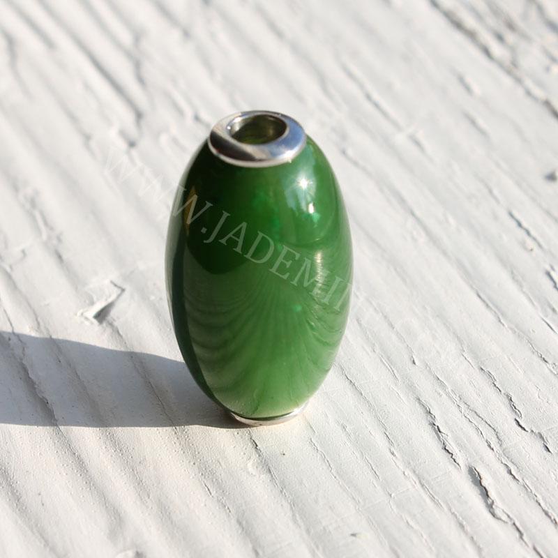 Green jade bead with top hole and metal ring, displayed upright on a white textured surface.