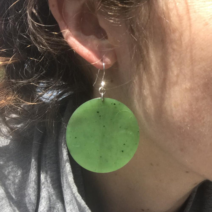 Green circular disc earring worn on the ear