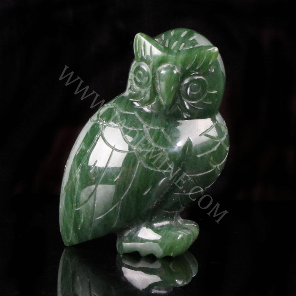 Green jade owl figurine carved with intricate feather patterns in a side view against a dark background