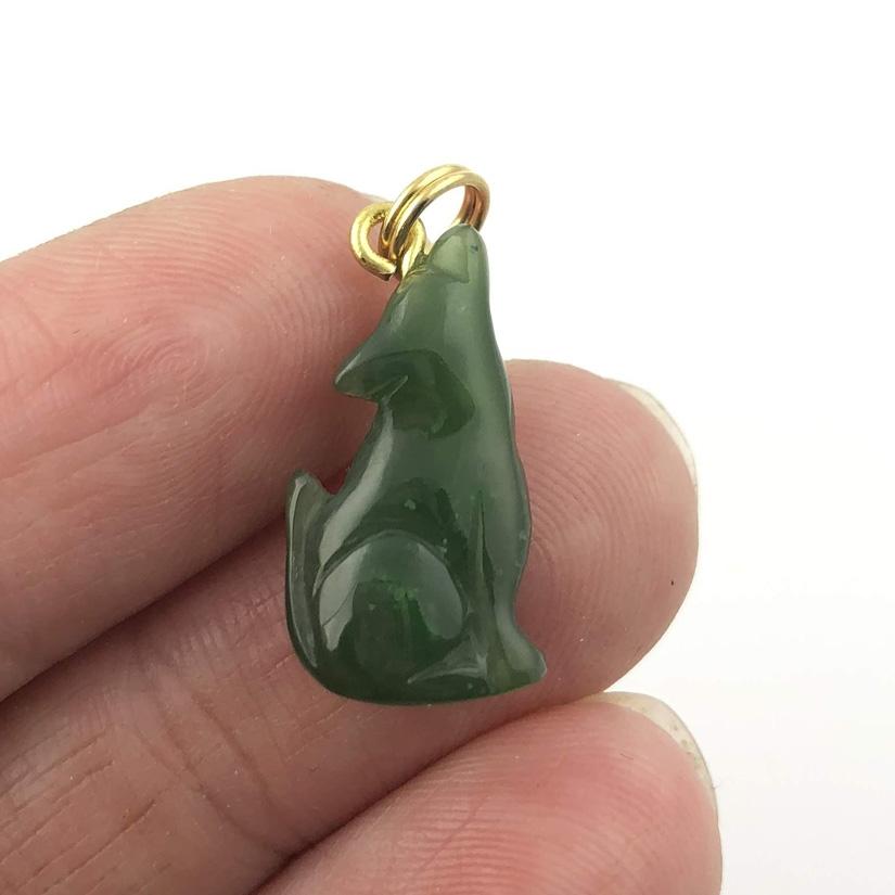 Green wolf pendant held between fingers showing its size and shape
