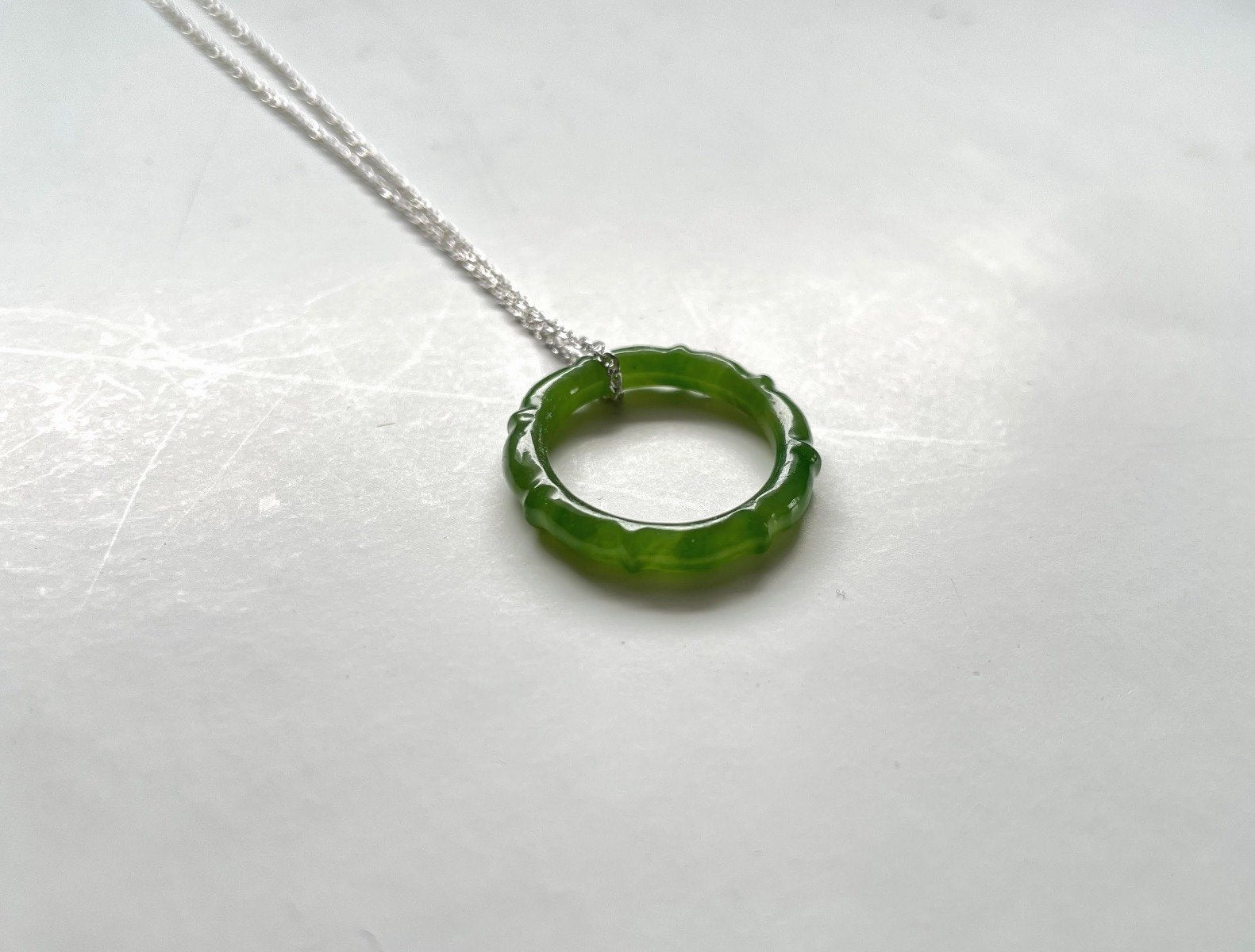 Circular green jade pendant with scalloped edge on a silver chain