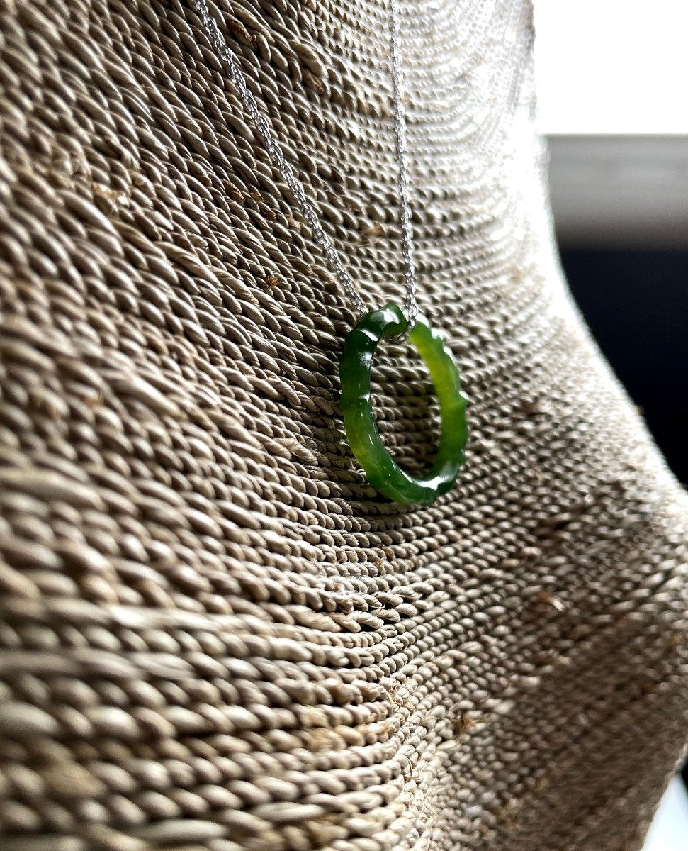 Green jade circular pendant on a silver chain resting against a woven bag background