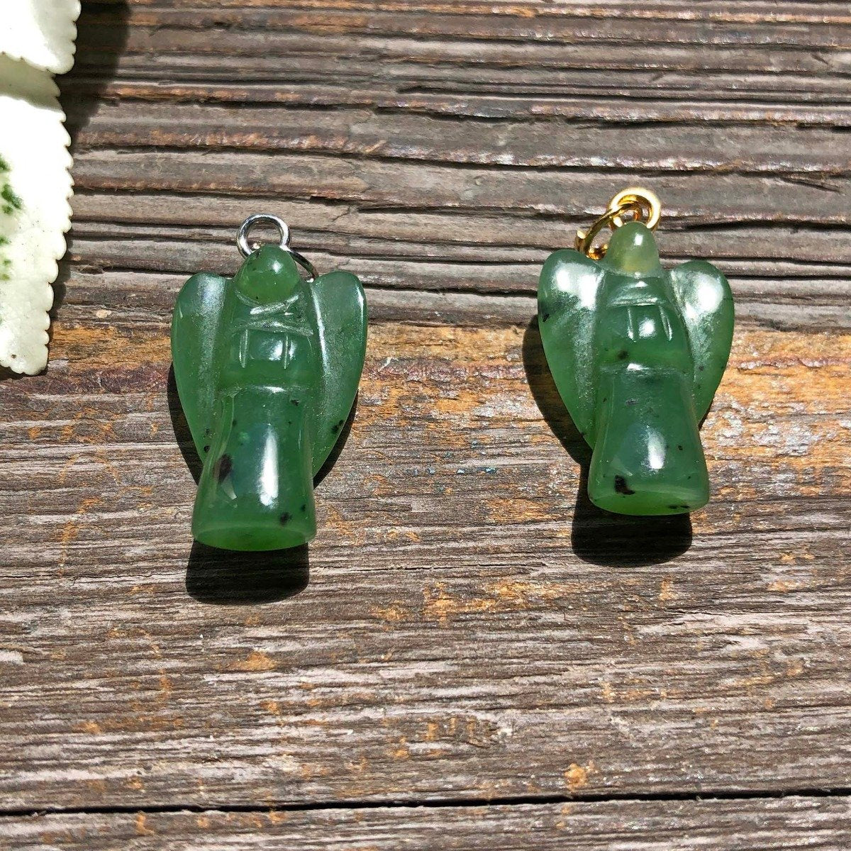 Two green jade angel charms with silver and gold loops on a wooden surface