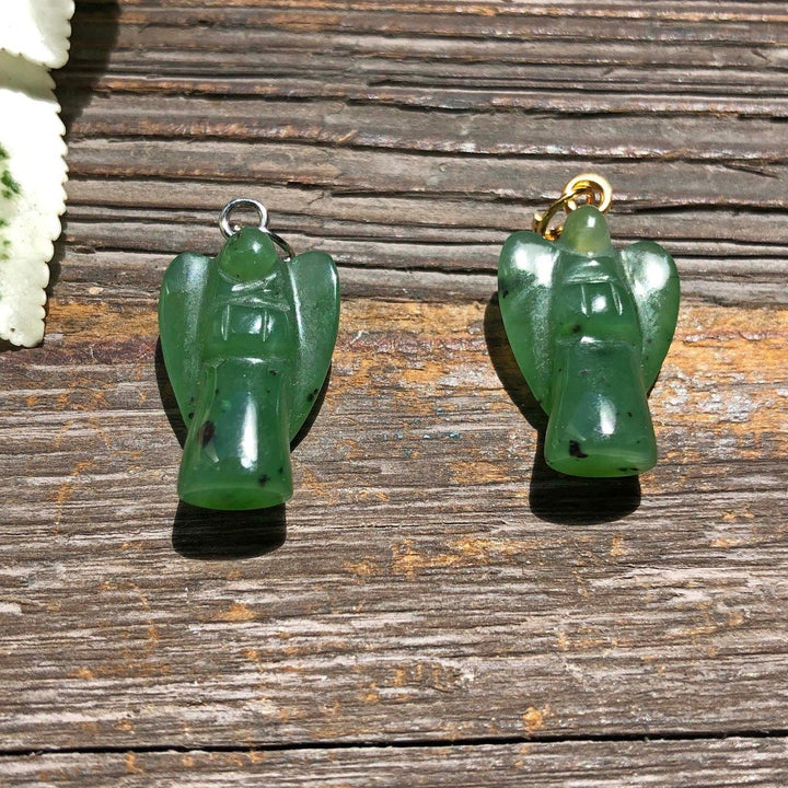 Two green jade angel charms with silver and gold loops on a wooden surface