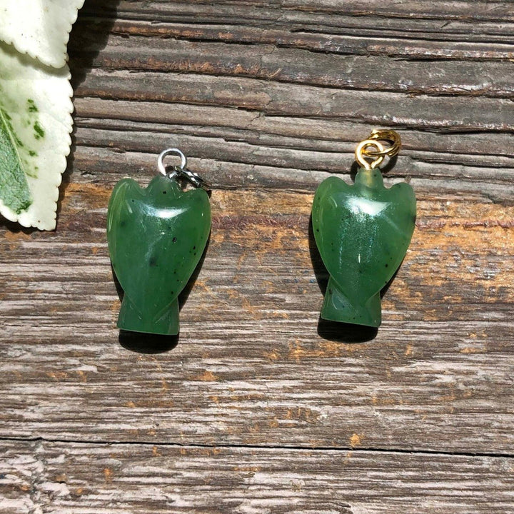 Green jade angel charms with silver and gold loops resting on a wooden surface