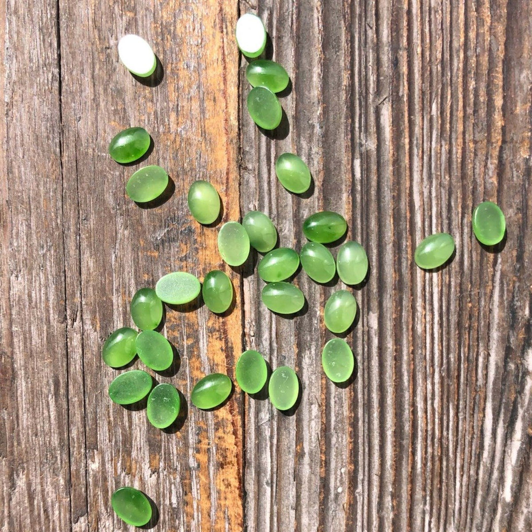 Green jade cabochons 5x7 mm scattered on a weathered wooden surface.