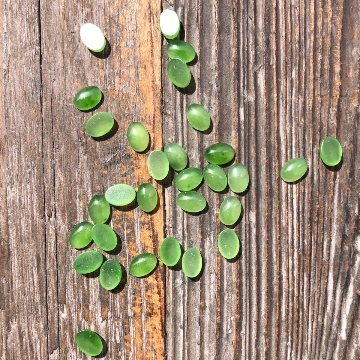 Green jade cabochons 5x7 mm scattered on a weathered wooden surface.