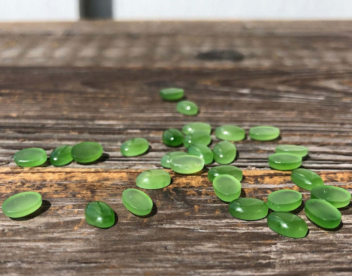 AA Canadian Jade Cabochons 5x7mm scattered on a rustic wooden surface