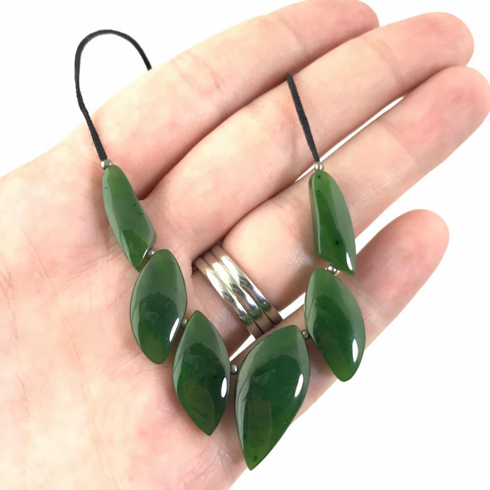 Jade necklace with glossy green leaf-shaped beads on a black cord held in the palm